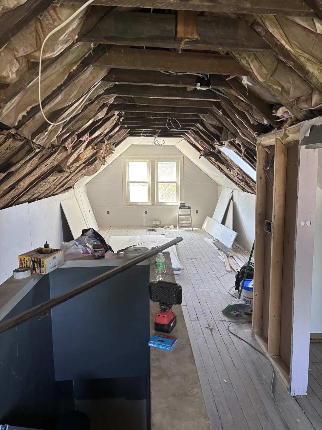 Attic room with new wall drywall and exposed ceiling rafters during installation.