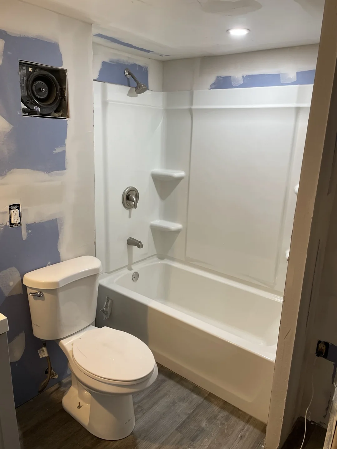 Bathroom tub and shower surround with nearby drywall patches and a toilet during renovation.