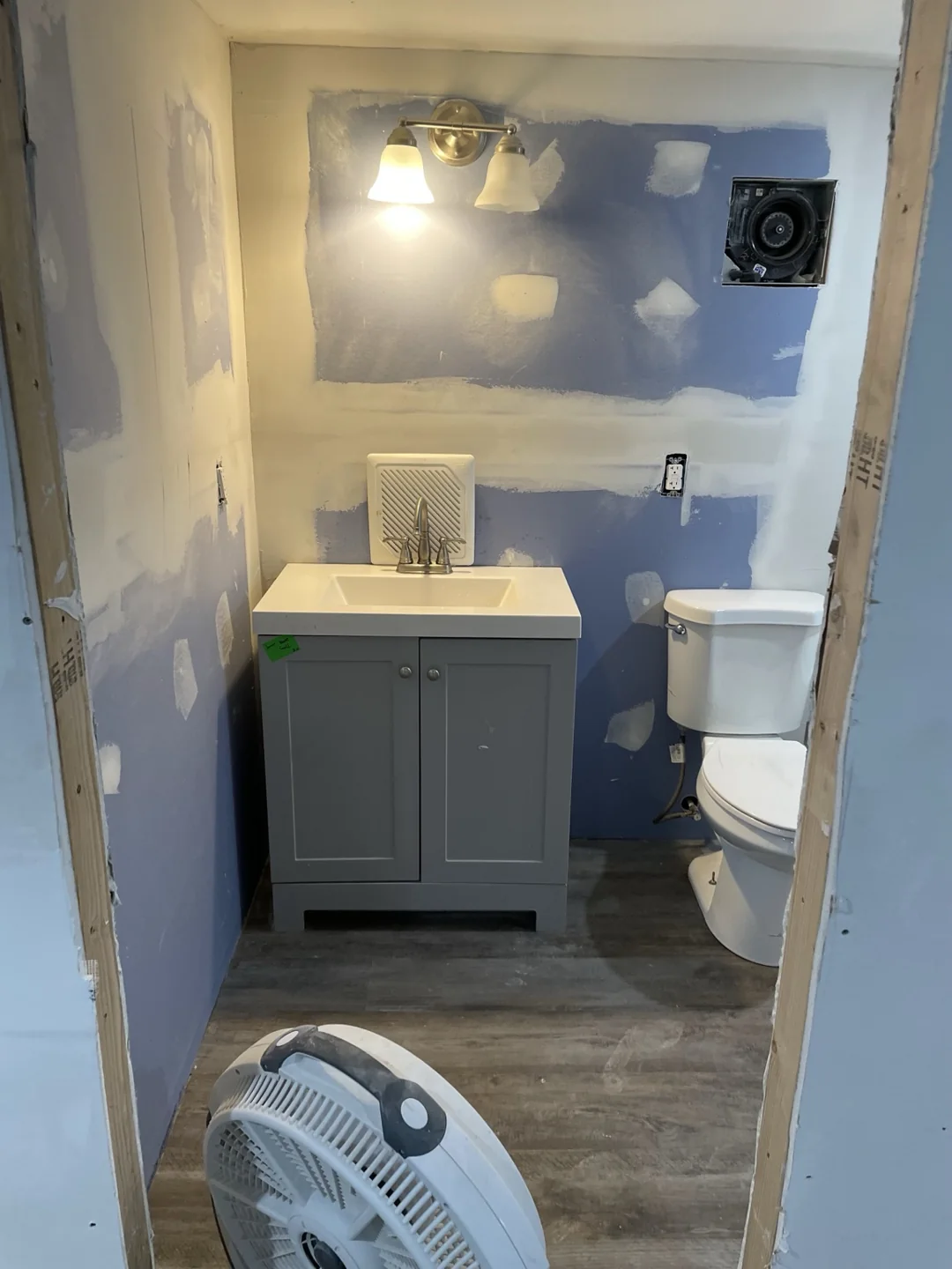 Gray bathroom vanity and sink with wood-look flooring, with wall finishing still in progress.