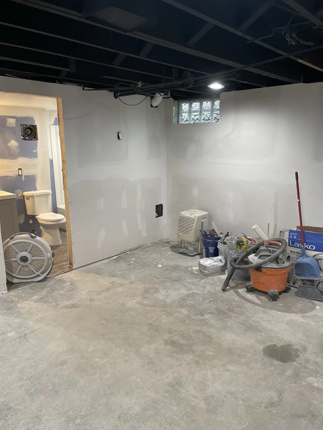 Basement room with drywall and joint compound, an exposed black ceiling and work materials.