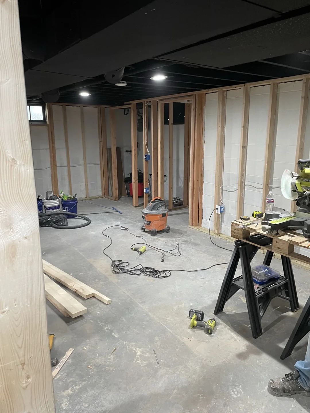 Basement room with new wall framing, exposed black ceiling joists and construction materials.