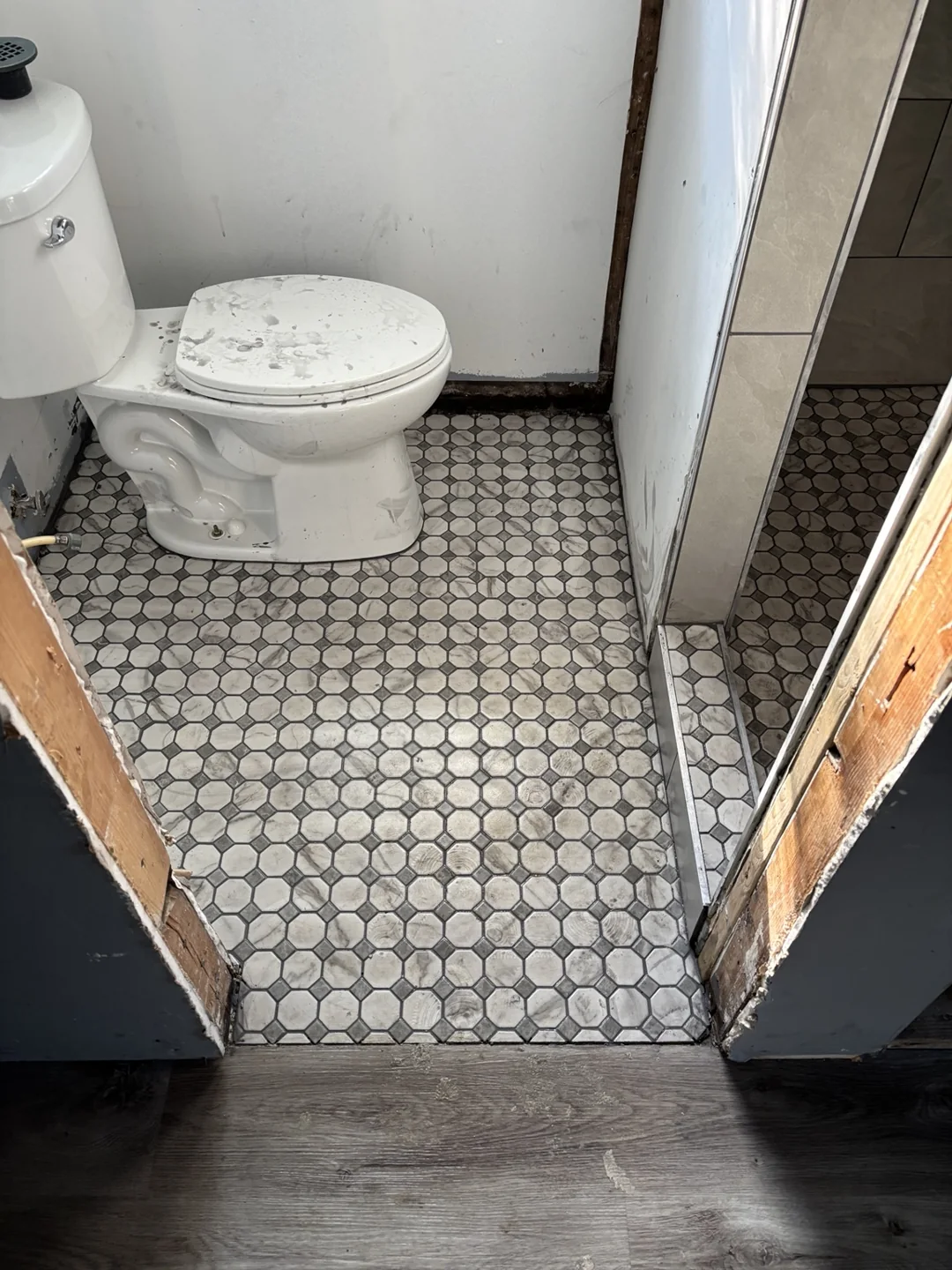 Gray and white mosaic bathroom floor tile around the toilet, with surrounding wall finishes still in progress.