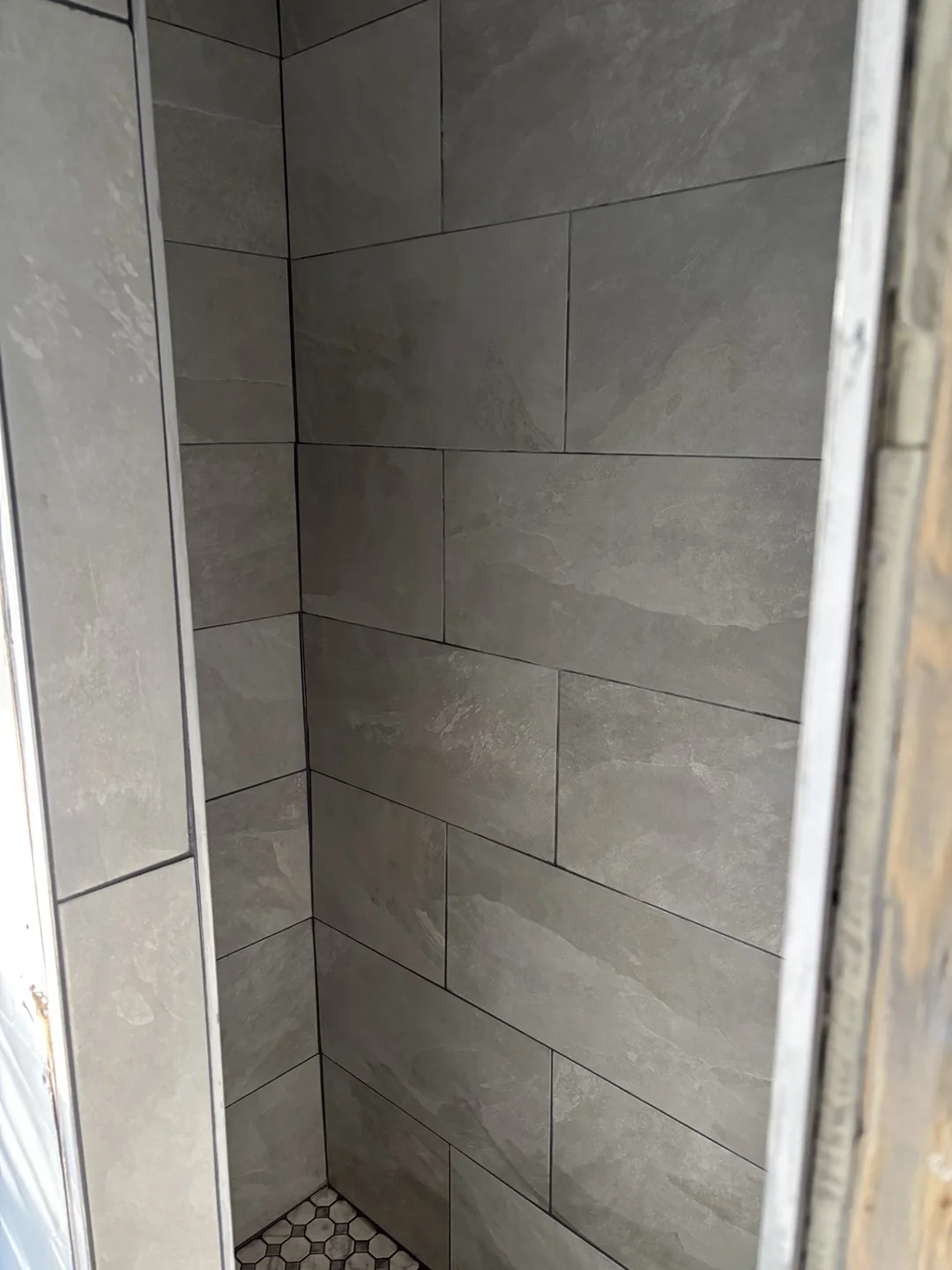 Large rectangular gray shower wall tiles above a mosaic shower floor during bathroom renovation.