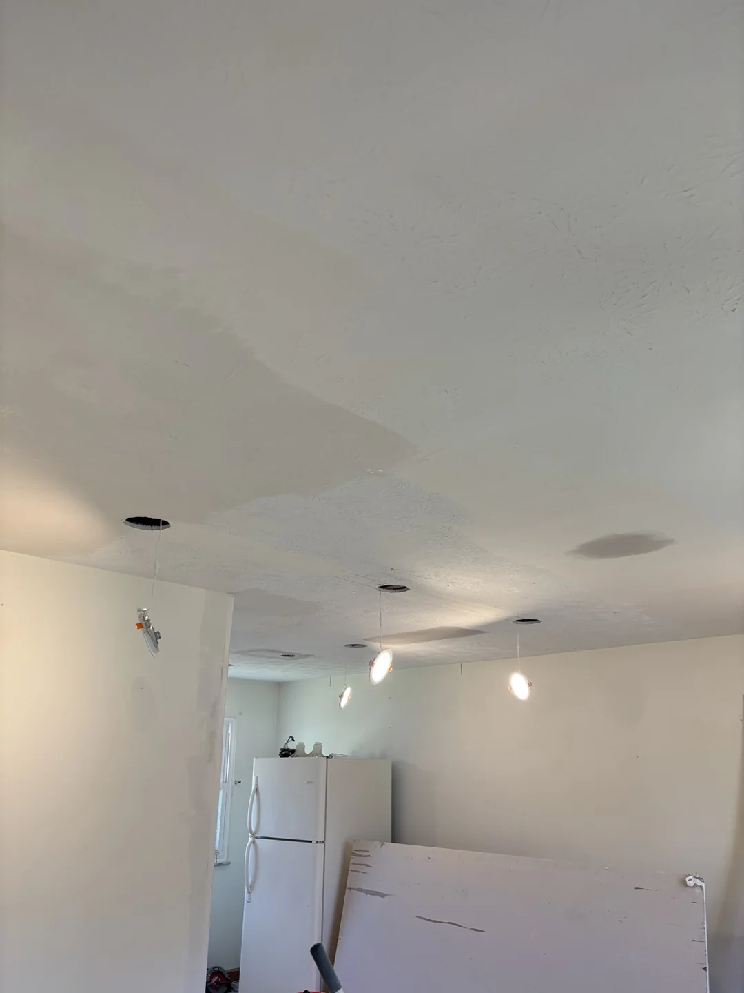 Ceiling smoothing in progress with LED downlights hanging below their openings during fitting.