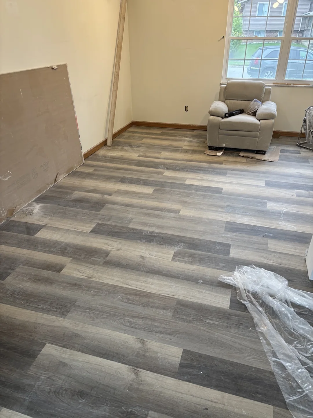 Installed gray wood-look plank flooring across the living room, with renovation materials still present.