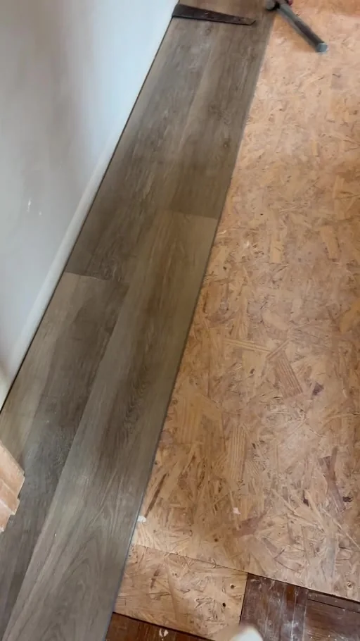 Video still showing wood-look plank flooring being installed over exposed subfloor.