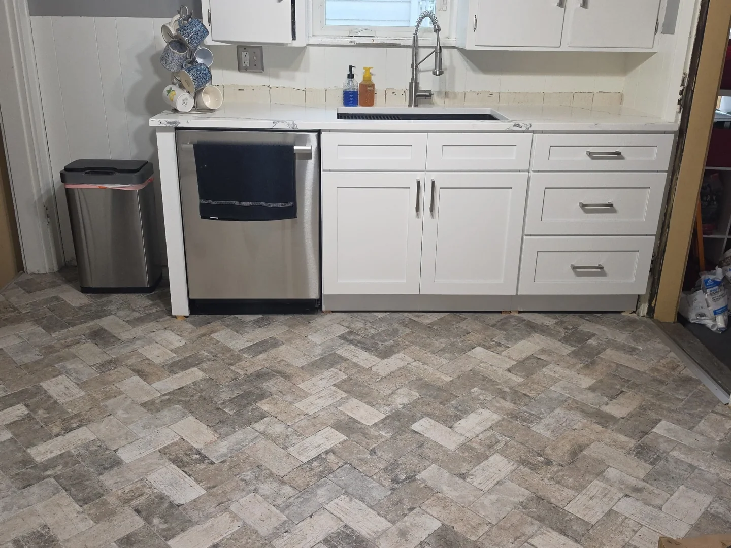 White kitchen base cabinets with handles, a countertop and sink above herringbone-pattern flooring.