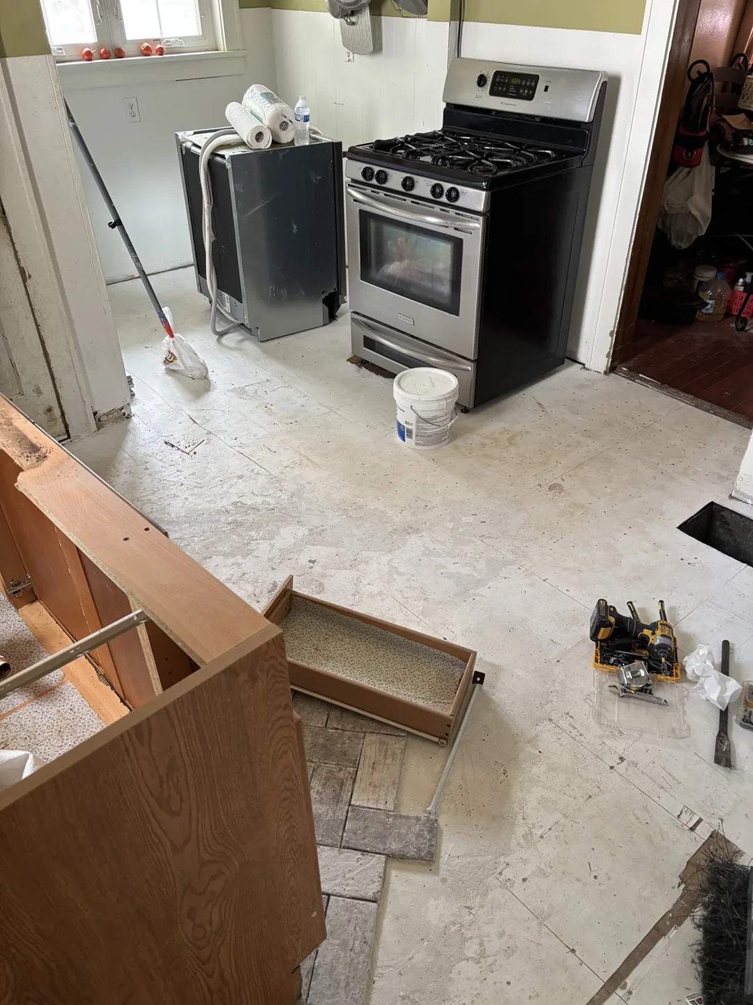 Kitchen during renovation with exposed floor surface, removed cabinetry and appliances moved aside.
