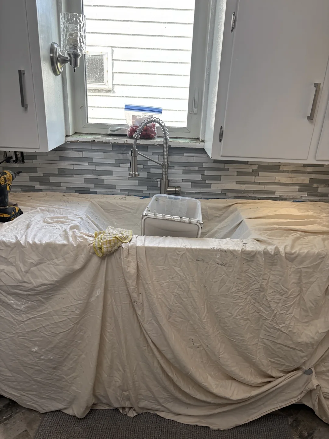 Gray mosaic kitchen backsplash behind the sink, with protective drop cloths covering the countertop during work.