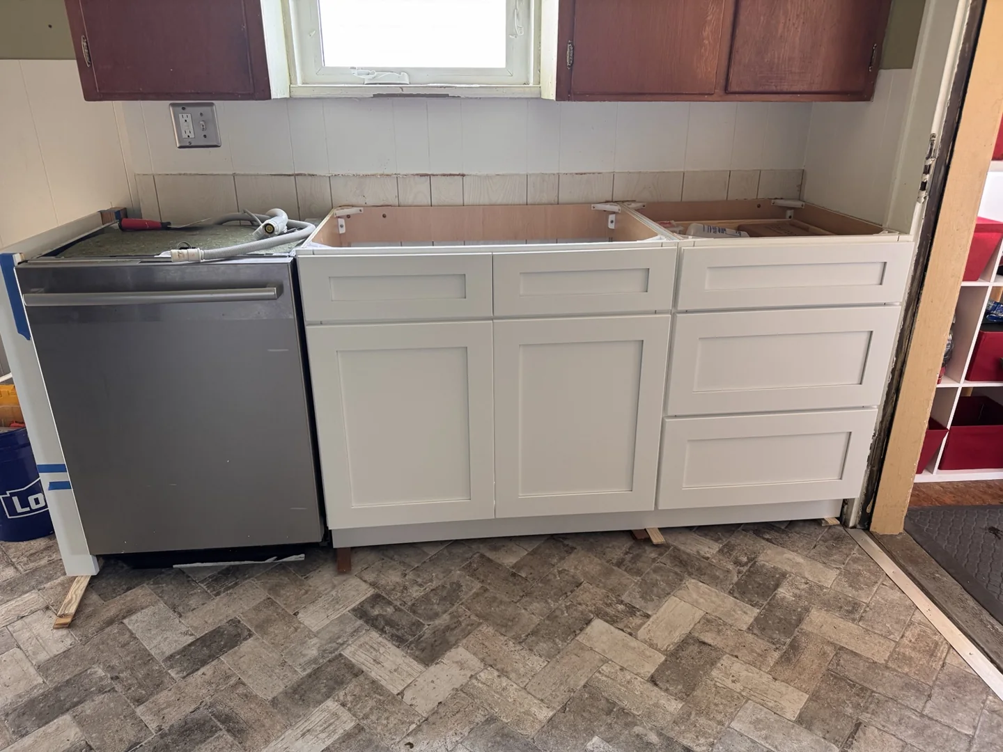 White base cabinets beside a dishwasher during installation, before the countertop and sink are fitted.