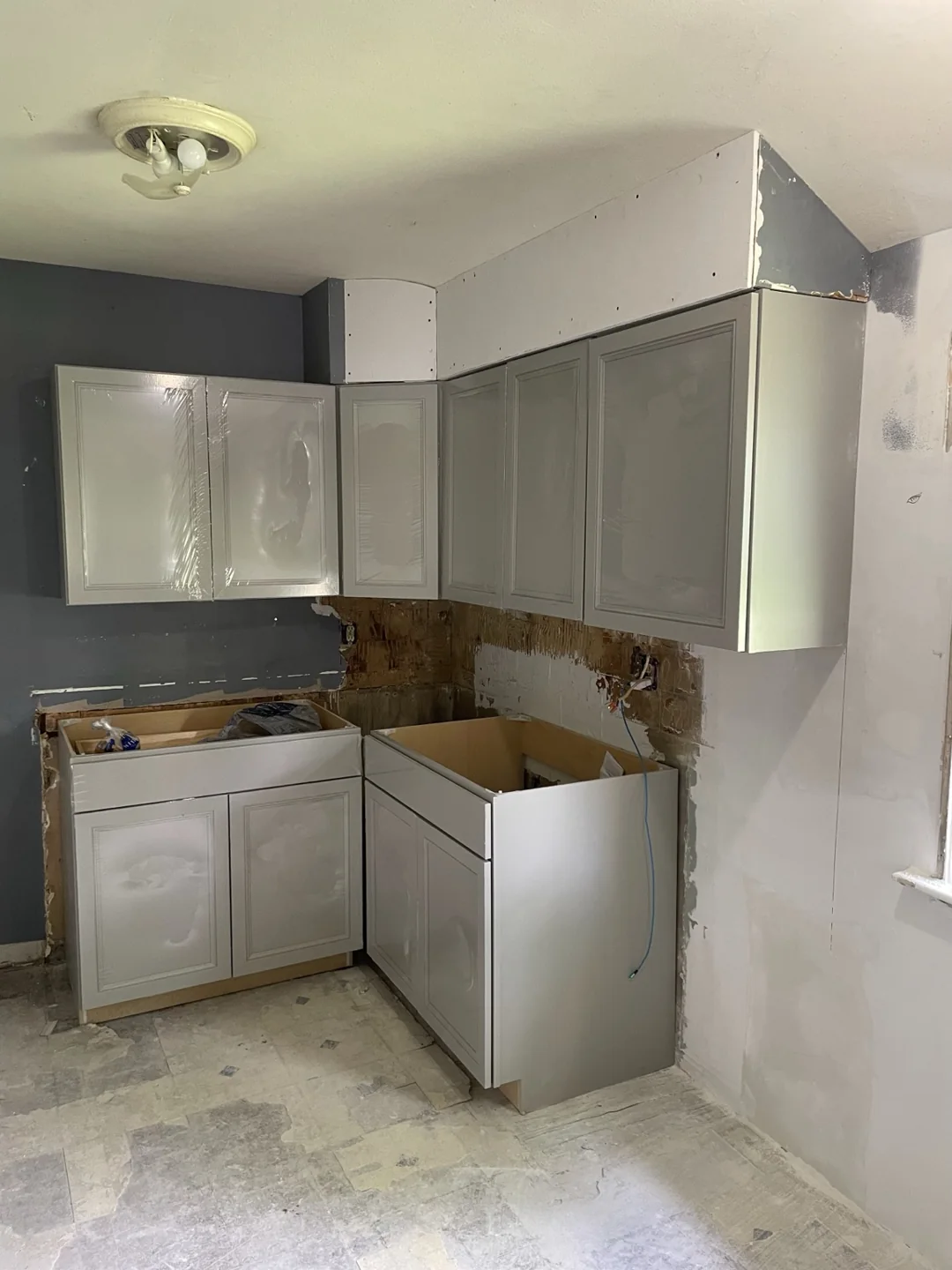 Gray upper and base cabinets installed around a kitchen corner, before countertops.