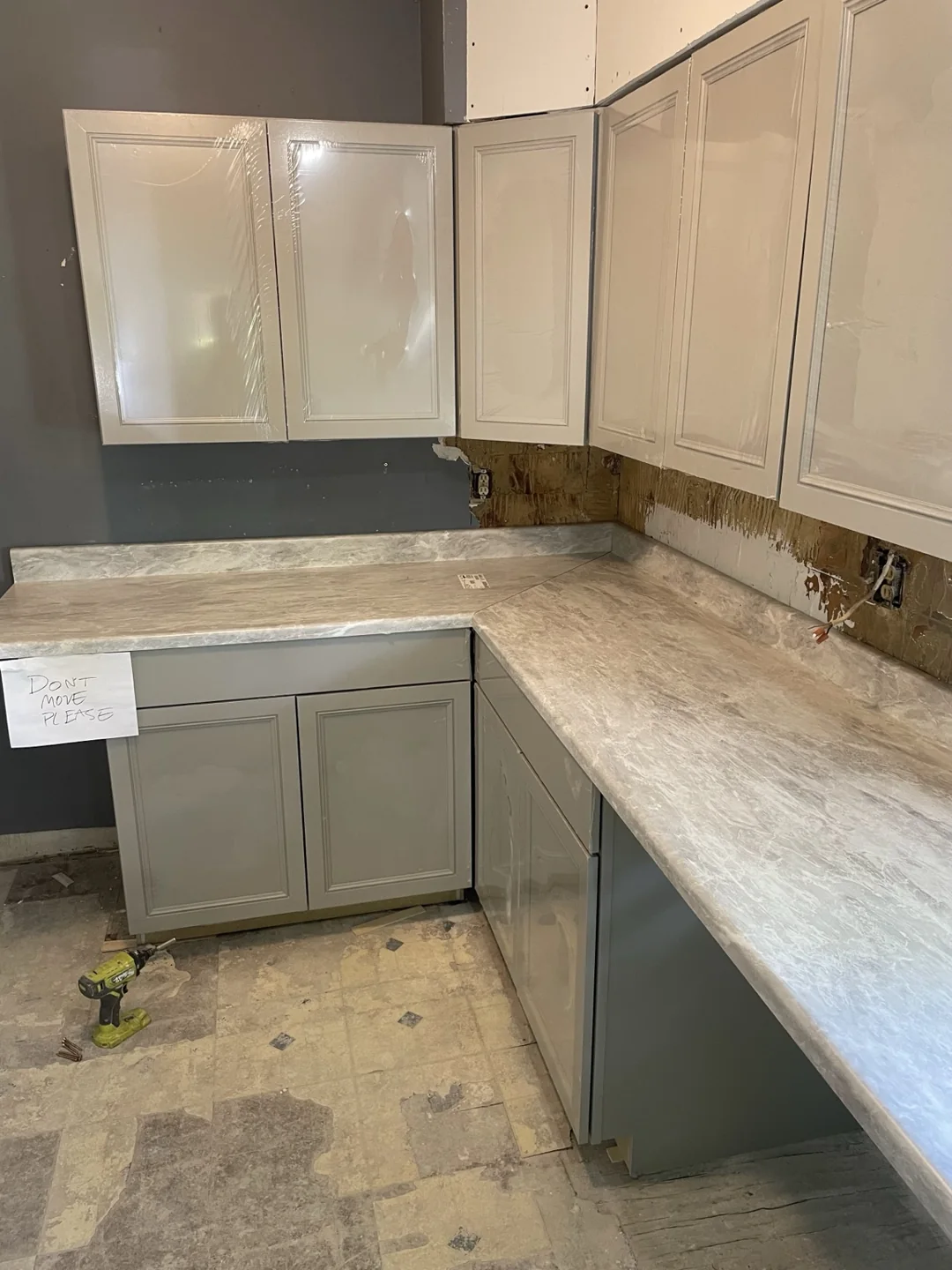 L-shaped kitchen countertop installed on gray base cabinets; wall finishing remains in progress.