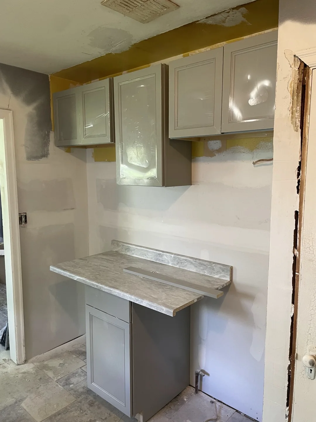 Countertop and gray cabinets along a newly drywalled kitchen wall, with finishing in progress.