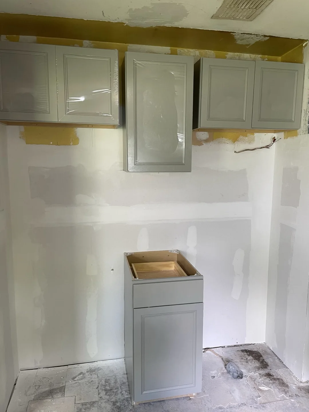 New drywall with taped seams beneath gray upper kitchen cabinets.