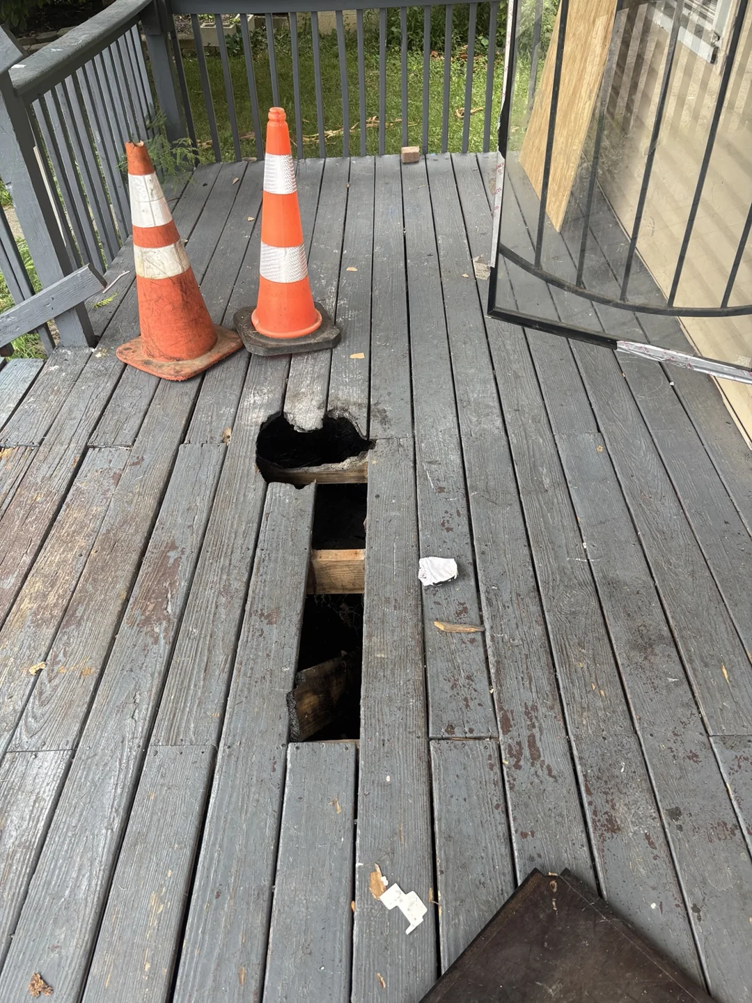 Damaged porch deck boards with a visible opening, marked by traffic cones.